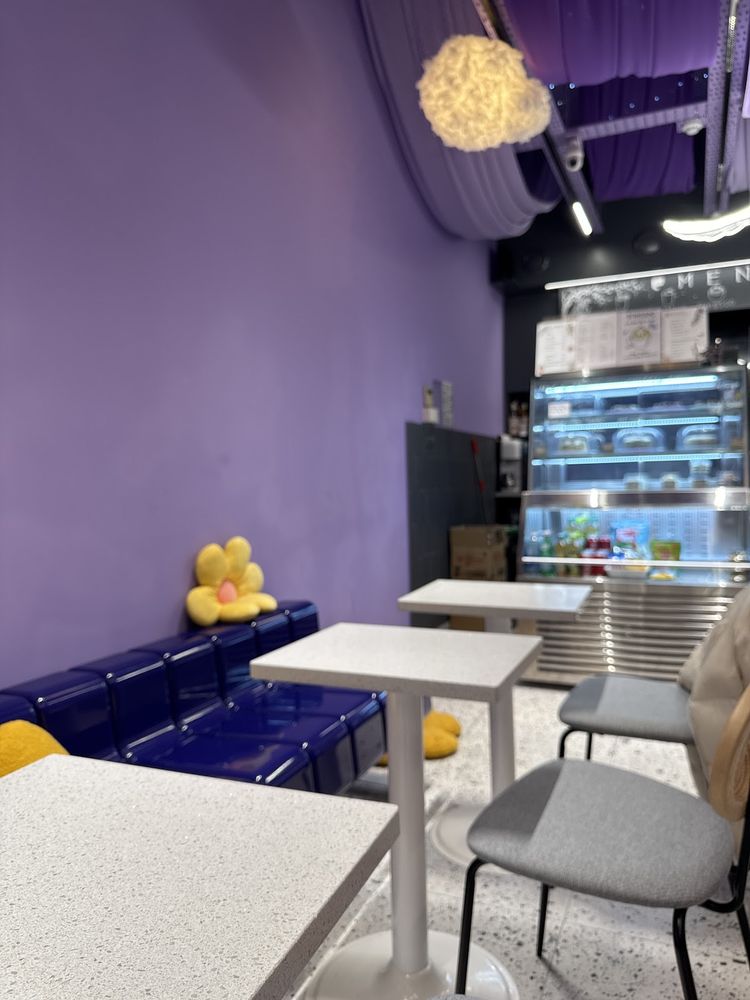 A corner of the purple dining room with white tables, grey chairs and a lit chilled cake display cabinet.